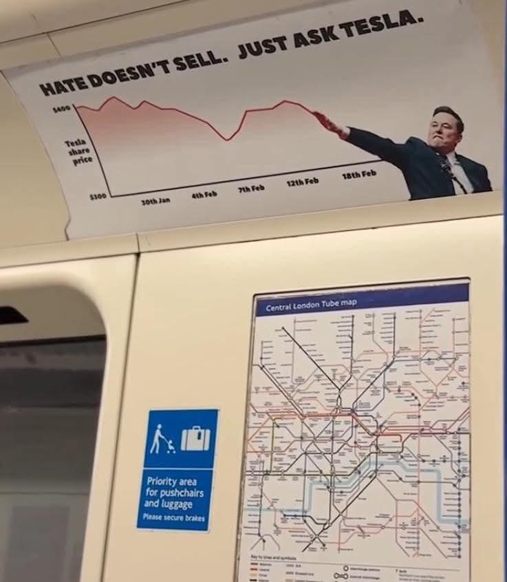 The picture shows the inside of a carriage on the London Underground. There are several notices on the wall. At the top is an advertising poster with the inscription "Hate doesn't sell. Just ask Tesla.". Below it is a graphic showing Tesla's falling share price. Elon Musk is pictured next to it, pointing to the falling line with his arm in Heil Hitler style. Below the poster is a sign for a priority area for pushchairs and luggage and a map of the London Underground network.