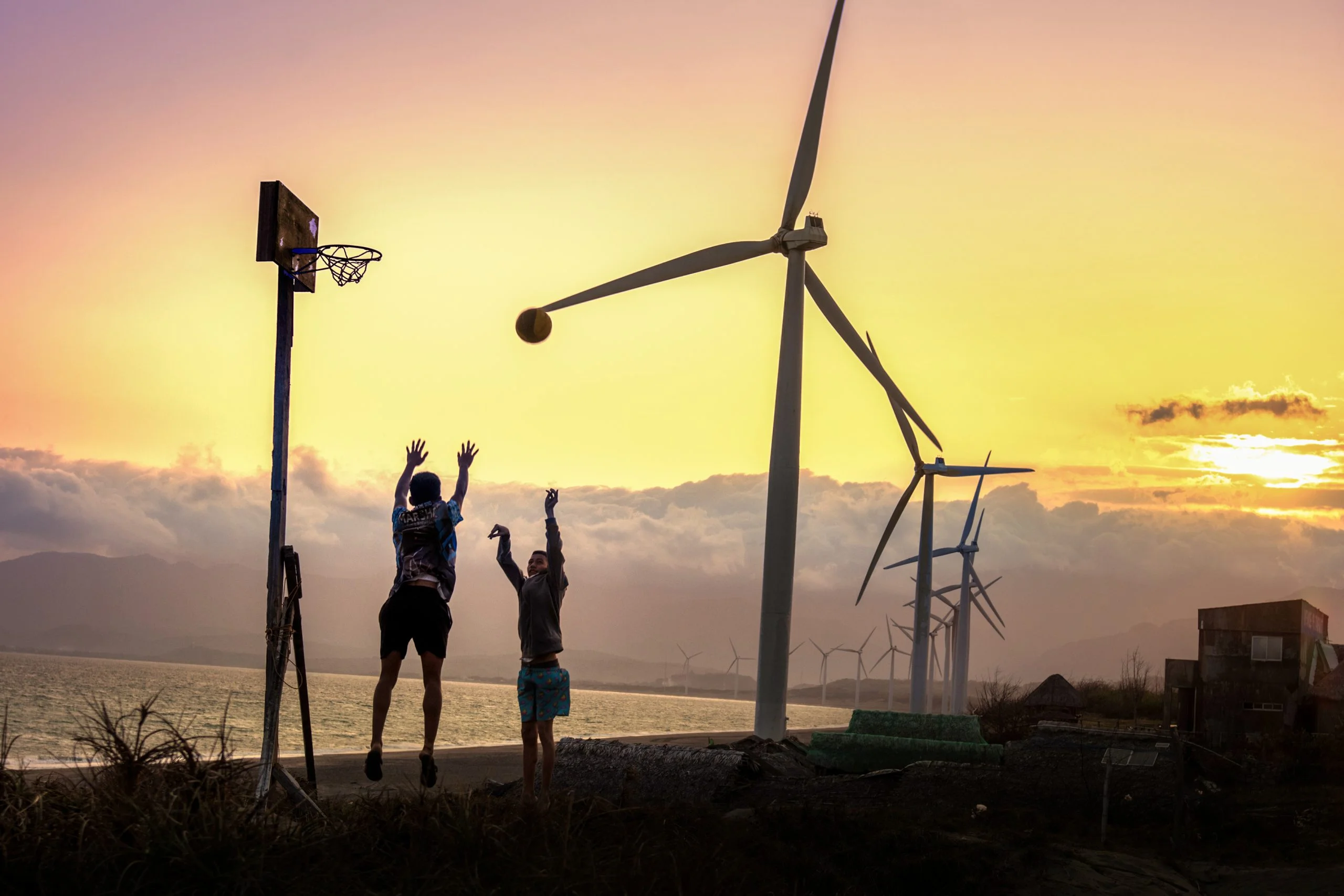 Two young people play basketball under the towering blades of the windmills in Bangui. The windmills lie along a 9-kilometer (5-mile) shoreline of Bangui Bay, facing the South China Sea. Renewable energy has transformed this community, cutting household expenses and powering opportunities once thought to be out of reach.