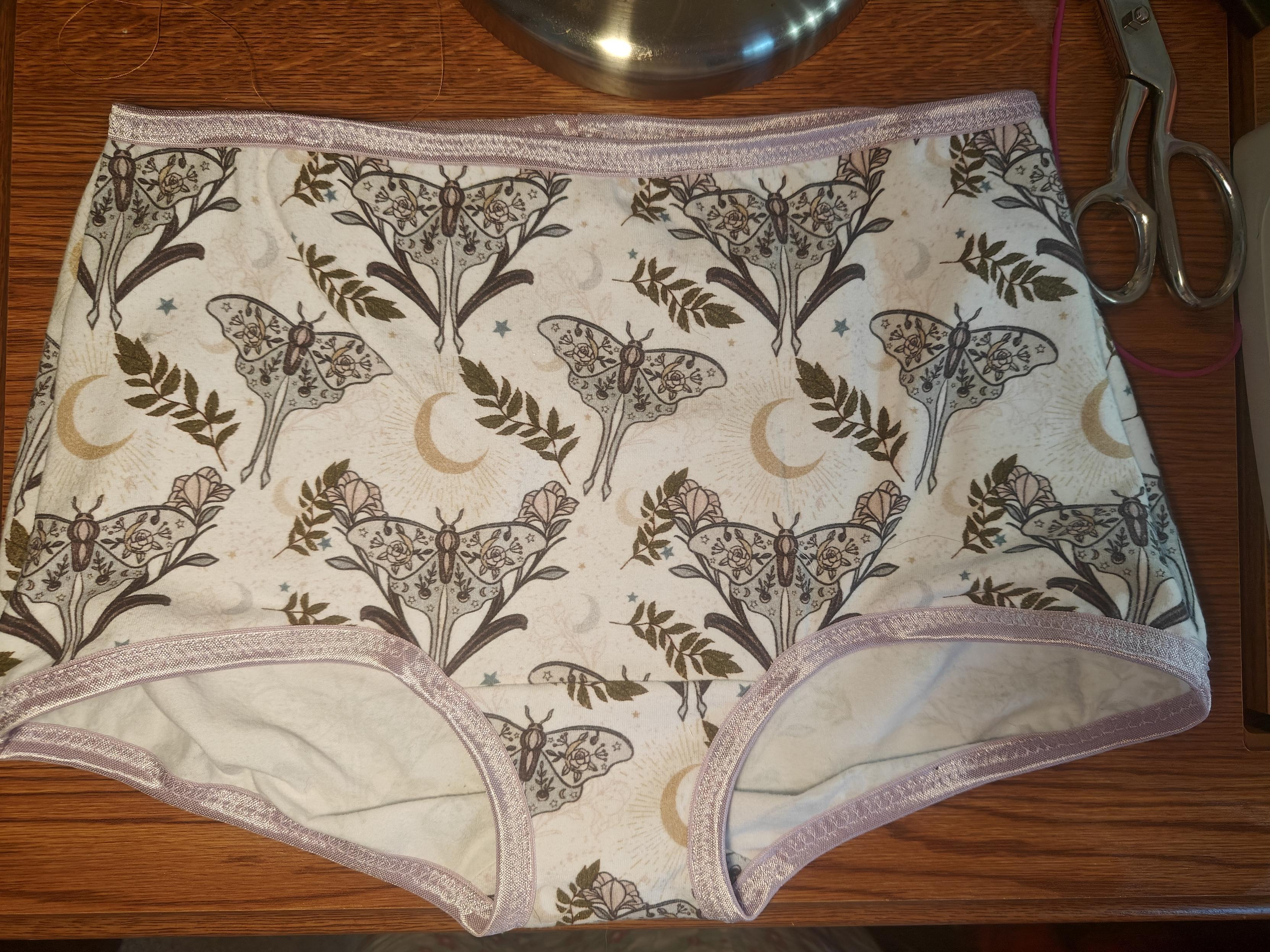 A pair of boy short underwear, white background, sage green and lavender moths, lavender leg and waist elastic 