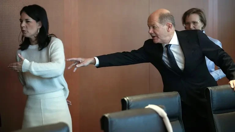 Chancellor Olaf Scholz reaches out in a gesture reminiscent of DaVinci's "Creation of Adam", while minister of foreign affairs Baerbock is turned away from him, making a dismissive gesture and starting to leave